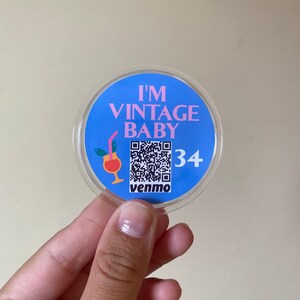 May include: A round, blue and pink sticker with the text "I'm Vintage Baby" and a QR code. The sticker also has a small illustration of a cocktail glass with a straw and the text "venmo" and "34".