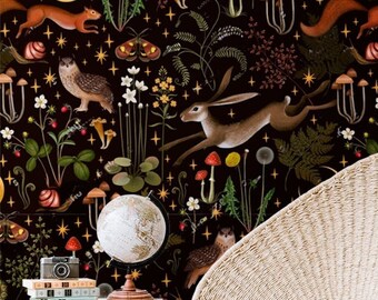May include: A cream-colored woven chair with black metal legs sits in front of a dark wallpaper. The wallpaper features a whimsical forest scene with owls, foxes, mushrooms, and a running hare. A small white side table holds a globe and books.