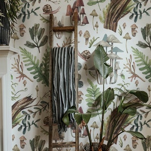 May include: A room with forest-themed wallpaper featuring mushrooms, ferns, and snails. A wooden ladder leans against the wall, with a striped blanket. A large potted plant with broad leaves sits in a woven basket.