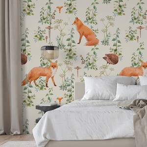 May include: Wallpaper featuring a repeating pattern of watercolor foxes, mushrooms, and greenery on a cream background. The design includes detailed illustrations of woodland elements, creating a nature-inspired aesthetic. The wallpaper is suitable for bedrooms and living spaces.