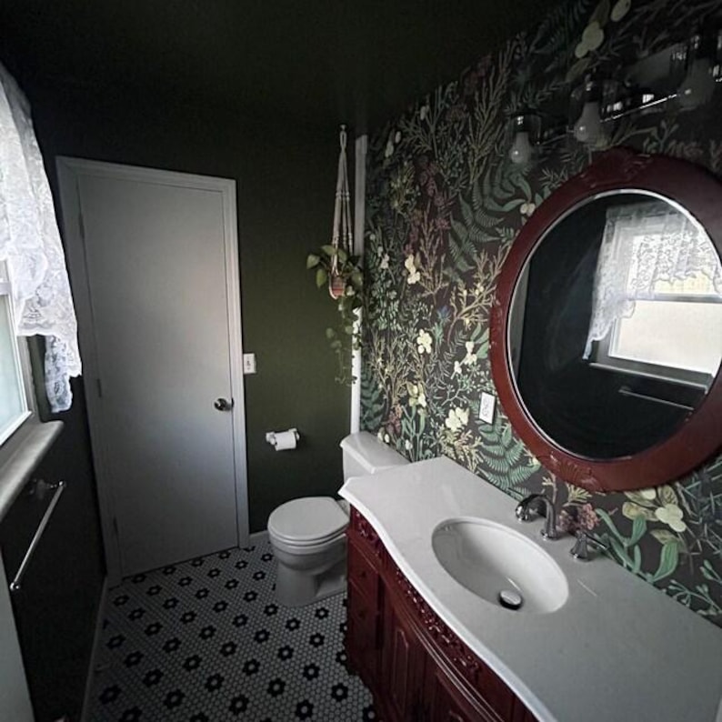 May include: A bathroom with dark green walls, floral wallpaper, and a dark wood vanity. A round mirror hangs above the vanity, and a white toilet and sink are visible. The floor has a black and white patterned tile.