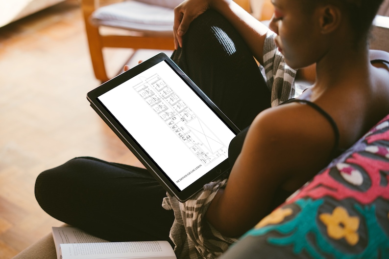 May include: A person sitting on a couch and looking at a tablet. The tablet screen shows a black and white architectural drawing of a building floor plan. The text on the tablet reads "THE DRAWINGS FOR THE FLOOR PLAN".