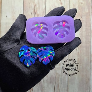 May include: Purple silicone mold with two leaf-shaped cavities. Two iridescent blue resin leaves are shown next to the mold. The text "Mini Machi." is printed on a black circle.