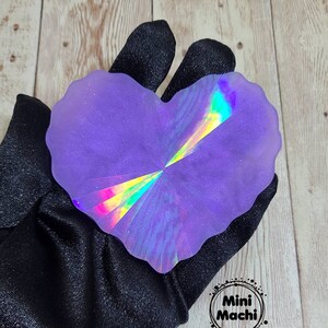 May include: A heart-shaped iridescent purple resin coaster with a holographic design. The coaster is on a black fabric background.