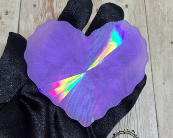 May include: A heart-shaped iridescent purple resin coaster with a holographic design. The coaster is on a black fabric background.