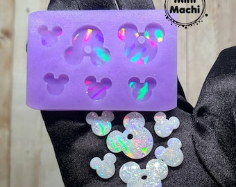 May include: A purple silicone mold with six Mickey Mouse head shapes. The mold is filled with iridescent glitter resin. There are also six finished resin Mickey Mouse head shapes with iridescent glitter.