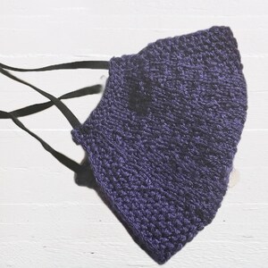 May include: A purple knitted face mask with black ties. The mask is made with a textured knit stitch.