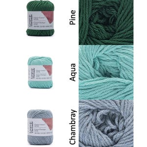 Op de afbeelding: Drie bollen Loops & Threads Classic Cotton garen in de kleuren Pine, Aqua en Chambray. Elke bol is voorzien van het merk, het garentype en 109 meter / 71 gram. Het garen is strak opgerold, wat de textuur en kleurvariaties laat zien.