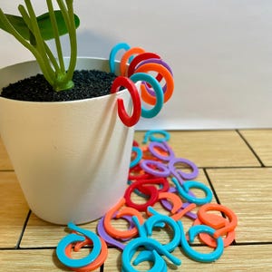 May include: A set of three ceramic mugs with a speckled, cream-colored glaze. Each mug features a different hand-painted design: a blue and green leaf, a yellow flower, and a red berry. The mugs have a simple, rounded shape.