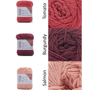 Op de afbeelding: Drie strengen Loops & Threads Classic Cotton garen in de kleuren tomaat, bordeaux en zalm. Elke streng is gelabeld met de merknaam, het garentype en de lengte-informatie. Het garen wordt in een close-up weergegeven, waarbij de textuur en kleurvariaties worden getoond.