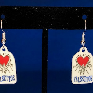 Peut inclure: Une paire de boucles d'oreilles blanches avec un motif de c&oelig;ur rouge et le mot "FALSETTOS" en bleu. Les boucles d'oreilles ont des crochets argent&eacute;s et un d&eacute;tail en forme de ressort. Le motif repr&eacute;sente un c&oelig;ur avec des personnages qui tendent la main.