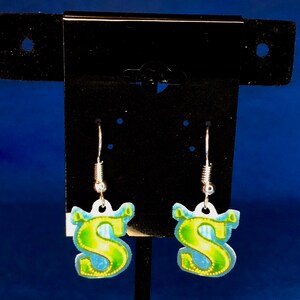 Peut inclure: Une paire de boucles d'oreilles pendantes avec la lettre "S" en vert et jaune, sur fond bleu. Les boucles d'oreilles sont suspendues &agrave; des crochets argent&eacute;s.