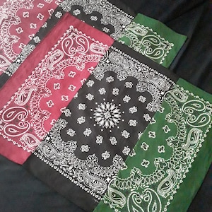 May include: Three bandanas folded in a stack, with a black bandana on top, a red bandana in the middle, and a green bandana on the bottom. Each bandana has a white paisley pattern.