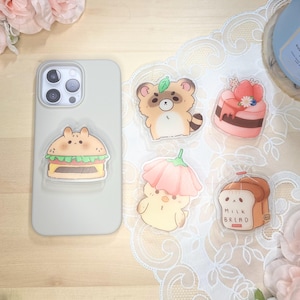 May include: A set of five clear phone case stickers featuring cartoon characters. The stickers include a raccoon, a burger, a chick with a flower, a cake, and a loaf of bread with the text "Milk Bread".