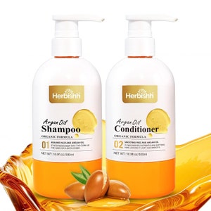 Puede incluir: Dos botellas de plástico blanco de champú y acondicionador de aceite de argán con etiquetas doradas. Las botellas están etiquetadas como "Argan Oil Shampoo" y "Argan Oil Conditioner" con la marca "Herbishh". Las botellas son de 500 ml.