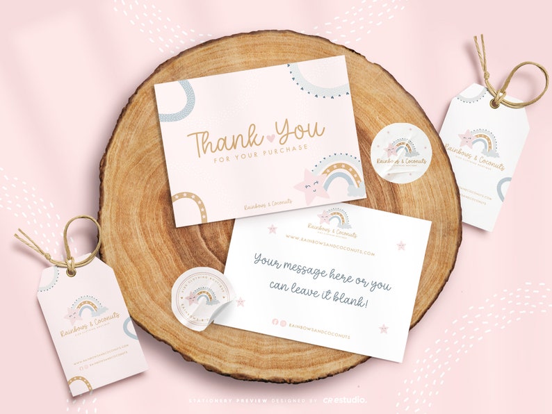 Op de afbeelding: Een briefpapier set met twee rechthoekige kaarten, twee ronde stickers en twee labels met touw. De items zijn wit met een pastelkleurig regenboog-, ster- en wolkenontwerp. De tekst bevat Thank You For Your Purchase en Rainbows & Coconuts.