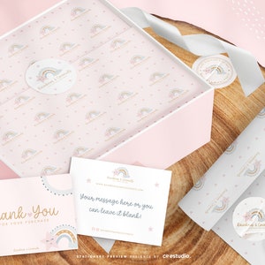 Op de afbeelding: Een lichtroze geschenkdoos bekleed met vloeipapier met een patroon van kleine regenbogen en sterren, vergezeld van twee witte kaarten. E&eacute;n kaart leest Thank You For Your Purchase, en de andere Your message here or you can leave it blank.