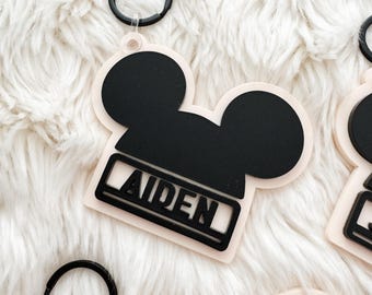 Könnte beinhalten: Ein weißer und schwarzer Mickey-Maus-Schlüsselanhänger mit einem schwarzen Ring und dem Namen "Aiden" in Schwarz.