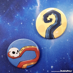 Könnte beinhalten: Zwei runde Ansteckbuttons. Ein Button zeigt einen dunkelblauen Tentakel auf gelbem Hintergrund. Der andere Button zeigt einen roten Tentakel, der einen kleinen weißen Totenkopf auf blauem Grund hält. Der Text "photo and artwork by BubbleBerry" ist sichtbar.