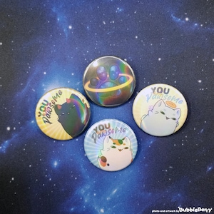 Könnte beinhalten: Vier bunte runde Knöpfe mit Katzenillustrationen und dem Text "You Pawsome" in verschiedenen Farben und Schriftarten.