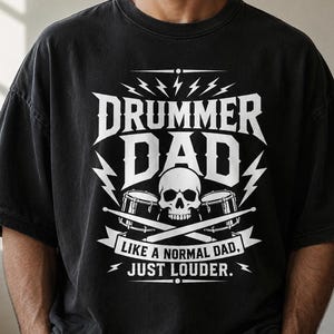 May include: Black t-shirt with the text "DRUMMER DAD" in white, featuring a skull, drumsticks, and drums. The text below reads "LIKE A NORMAL DAD, JUST LOUDER."