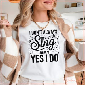 May include: White t-shirt with the text "I DON'T ALWAYS SING...OH WAIT YES I DO" in black. The word "Sing" is in a stylized font with musical notes around it. The shirt is being worn by a person with blonde hair, a gold necklace, and a brown and white cardigan.