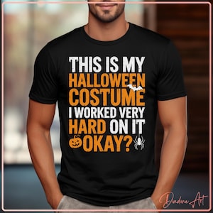 May include: Black t-shirt with the text "THIS IS MY HALLOWEEN COSTUME I WORKED VERY HARD ON IT OKAY?" in white and orange. The design includes a bat, pumpkin, and spider. A Halloween-themed graphic tee.