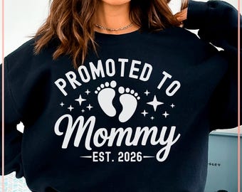 May include: Black sweatshirt with the text "PROMOTED TO Mommy EST. 2026" in white. The design includes baby footprints and stars. A casual top for expecting mothers.