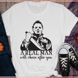 May include: White t-shirt with a black and white graphic of a man holding a knife. The text "A real man will chase after you" is printed below the graphic.