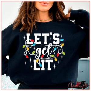 May include: Black sweatshirt with the text "LET'S get LIT" in white, decorated with colorful string lights. The design includes red, yellow, and blue lights, and small white stars. A festive holiday-themed apparel item.