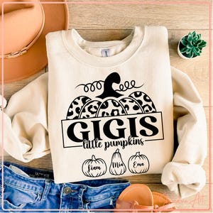 May include: Cream-colored sweatshirt with a black pumpkin design. The pumpkin has leopard print sections and the text "GIGIS little pumpkins". Below the text are three pumpkin illustrations with names: Fiam, Mia, and Ema.