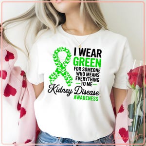 May include: White t-shirt with a green ribbon made of butterflies and the text "I Wear Green for Someone Who Means Everything to Me - Kidney Disease Awareness". The shirt is a crew neck style.
