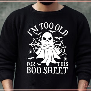 May include: Black crew neck sweatshirt with a white graphic. The graphic features a grumpy ghost with crossed arms, spiderwebs, bats, and the text "I'M TOO OLD FOR THIS BOO SHEET". A fun Halloween-themed design.