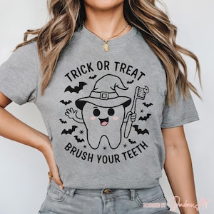 May include: A grey t-shirt with a Halloween graphic. The design shows a cartoon tooth in a witch's hat holding a toothbrush, with bats around it. The text says "Trick or Treat Brush Your Teeth".
