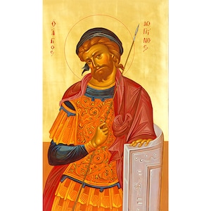 Könnte beinhalten: Eine byzantinische Ikone, die einen männlichen Heiligen in einem roten und goldenen Gewand darstellt, der eine Lanze hält. Die Ikone ist auf goldenem Hintergrund mit einem Heiligenschein um den Kopf des Heiligen gemalt. Der Text "Ο ΑΓΙΟΣ" ist in Griechisch auf der linken Seite der Ikone geschrieben.