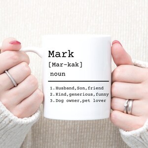 May include: White ceramic mug with a black design that says "Mark [Mar-kak] noun 1. Husband, Son, friend 2. Kind, generous, funny 3. Dog owner, pet lover"