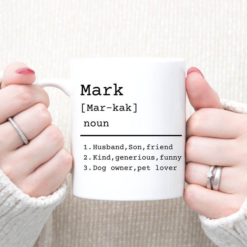 May include: White ceramic mug with a black design that says "Mark [Mar-kak] noun 1. Husband, Son, friend 2. Kind, generous, funny 3. Dog owner, pet lover"