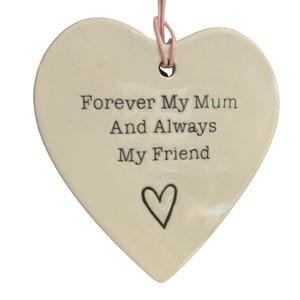May include: White ceramic heart-shaped ornament with a pink ribbon hanging from the top. The ornament has the text "Forever My Mum And Always My Friend" and a small heart at the bottom.