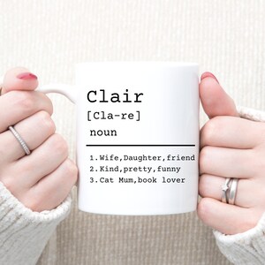 May include: White ceramic mug with black text that reads "Clair [Cla-re] noun 1. Wife, Daughter, friend 2. Kind, pretty, funny 3. Cat Mum, book lover"
