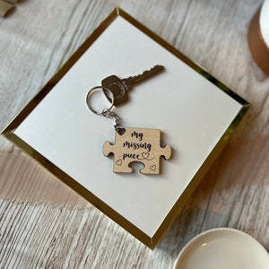 May include: A wooden puzzle piece keyring with the text "my missing piece" and a heart design. The keyring is attached to a silver key ring.