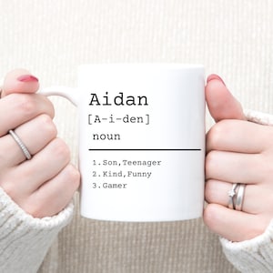 May include: White ceramic mug with a black design that says "Aidan [A-i-den] noun 1. Son, Teenager 2. Kind, Funny 3. Gamer"