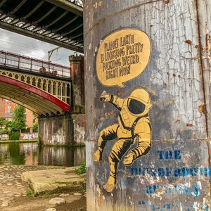 May include: A yellow and black sticker on a gray concrete pillar with a drawing of an astronaut and the text "Planet Earth is looking pretty fucking weird right now".