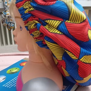 Könnte beinhalten: Eine blaue, rote und gelbe gemusterte Satin-Mütze mit einem gerafften Gummiband. Die Mütze wird auf einem Mannequin-Kopf getragen.