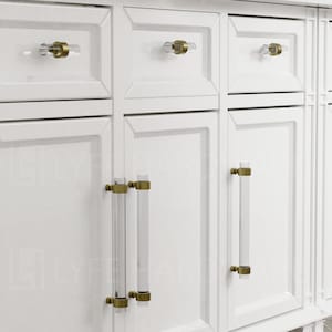 May include: White cabinet doors with clear acrylic and brass cabinet pulls. The cabinet doors have a raised panel design.