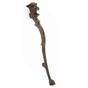 May include: A cast iron fireplace tool with a decorative animal head at the top and a paw at the bottom. The tool is brown and has a curved shape.