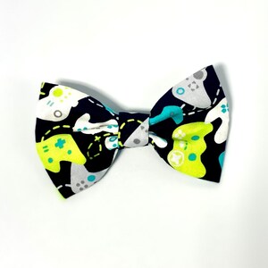 May include: A black bow tie with a pattern of white, green, and blue video game controllers.