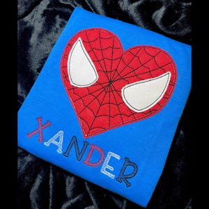 May include: Blue t-shirt with a red and black heart-shaped Spider-Man design and the name "Xander" in colorful letters.