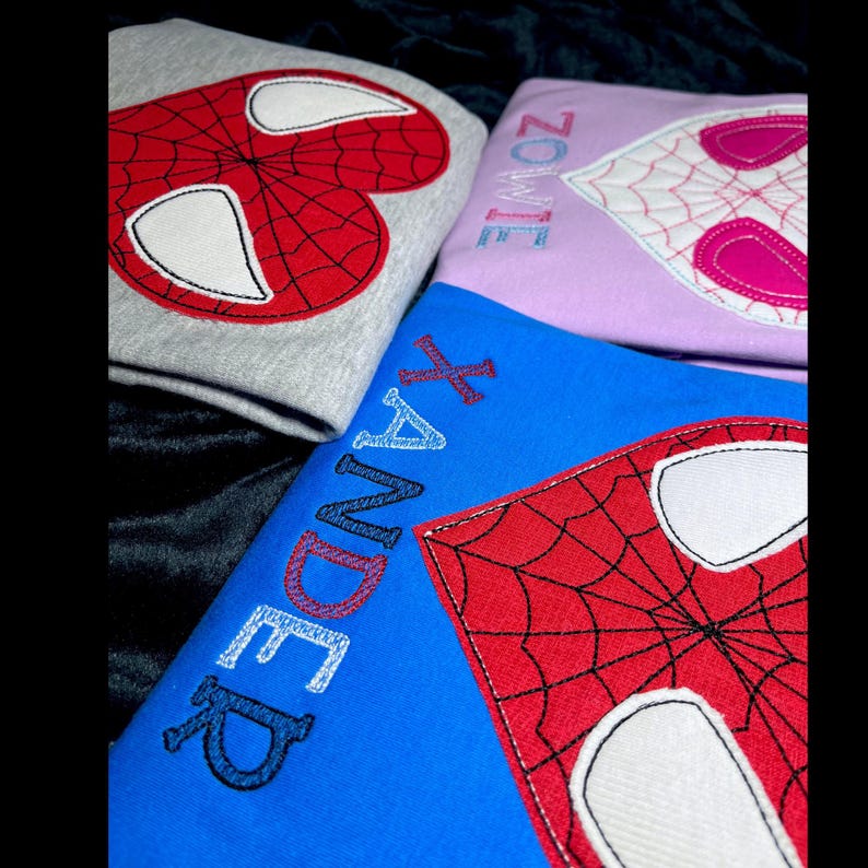 May include: Three blue, gray, and purple shirts with embroidered Spiderman logos and names. The blue shirt says "Xander" in rainbow colors, the gray shirt has a red and white Spiderman logo, and the purple shirt says "Zoey" in blue and pink.
