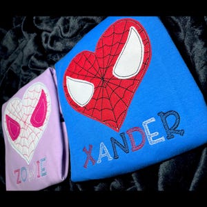 May include: Two light blue t-shirts with embroidered red and white spider-man hearts and the names "Xander" and "Zowie" in colorful letters.