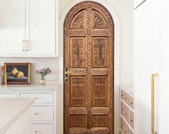 May include: A carved wooden door with an arched top and intricate details. The door is painted in a warm brown color and has a brass door handle.